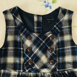 May include: A sleeveless plaid dress in navy, light blue, and white. The dress features a double-breasted design with six brown buttons and a round neckline. The Tommy Hilfiger label is visible.