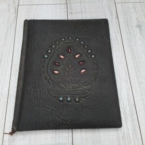 May include: A dark brown leather-bound journal with a decorative embossed design of a tree with pink and red beads on the front cover.