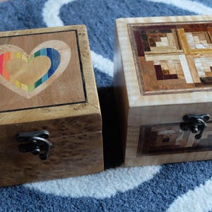 May include: Two wooden boxes with intricate inlaid designs. One box features a rainbow heart design, while the other has a geometric pattern.