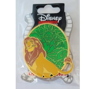 May include: A gold-colored pin featuring Simba from Disney's The Lion King. Simba is sitting with a green background of the jungle. The pin is round and has the Disney Studio Store logo at the top.
