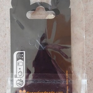 May include: A black and white pin with a Mickey Mouse head silhouette and the text "disneylandparis.com" on a black background. The pin is packaged in a clear plastic bag with a black header card that has a Mickey Mouse head silhouette and the text "Disney - Made in China".