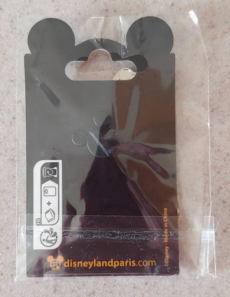 May include: A black and white pin with a Mickey Mouse head silhouette and the text "disneylandparis.com" on a black background. The pin is packaged in a clear plastic bag with a black header card that has a Mickey Mouse head silhouette and the text "Disney - Made in China".