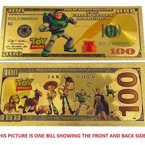 K&ouml;nnte beinhalten: Ein goldfarbener Papier-Geldschein mit Toy Story-Motiv. Die Vorderseite zeigt Buzz Lightyear, die R&uuml;ckseite Woody und die anderen Toy Story-Charaktere. Der Schein tr&auml;gt auf der R&uuml;ckseite die Aufschrift "24K Gold" und "Toy Story".