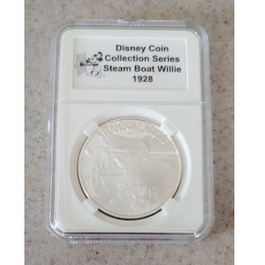 May include: A silver coin in a plastic case with a white label that reads "Disney Coin Collection Series Steam Boat Willie 1928". The coin features a depiction of Mickey Mouse in his Steamboat Willie role.