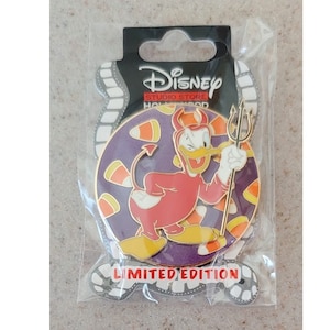 May include: A round, purple and gold Disney Studio Store Hollywood pin featuring a cartoon devil duck holding a trident. The pin is surrounded by candy corn and the text "LIMITED EDITION".