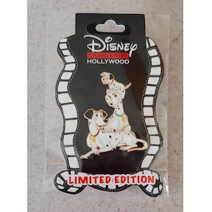 May include: A black and white Dalmatian dog pin with a smaller Dalmatian puppy on its back. The pin is on a black background with white film strips around the edges. The text "Disney Studio Store Hollywood" is at the top of the pin and "Limited Edition" is at the bottom.
