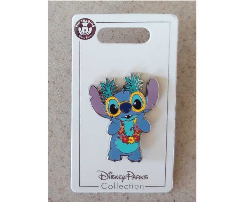 May include: Blue Stitch character wearing yellow sunglasses and a flower lei. The pin is on a white card with the text "Disney Parks Collection".