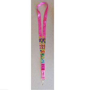 May include: Pink lanyard with a white polka dot pattern and a colorful image of Disney princesses. The lanyard has a plastic clasp and a metal ring.