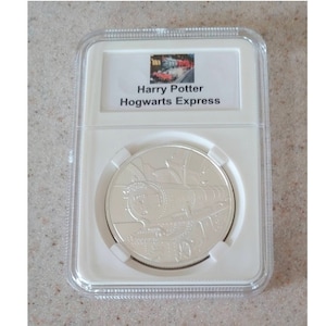 May include: A silver coin in a plastic case with a picture of the Hogwarts Express train. The coin has the text "Harry Potter Hogwarts Express" on the label.