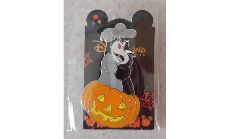 May include: A silver pin featuring a cartoon black cat sitting on top of an orange jack-o'-lantern. The pin has a black background with the text "Disneyland Paris" and a spider web design.