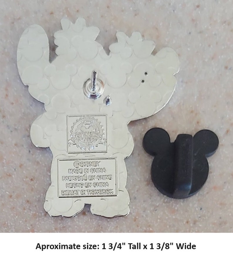 May include: Silver-toned metal pin featuring Stitch from Lilo & Stitch. Stitch is wearing a red Santa hat and holding a gift. The pin is approximately 1 3/4 inches tall and 1 3/8 inches wide. The back of the pin has the Disney logo and "Made in China" printed on it.