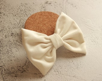 May include: A large, off-white velvet bow with a center loop. The bow is lying on a light brown, textured surface.