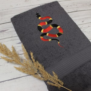 Peut inclure: Une serviette de bain grise avec un motif de serpent brodé en rouge, jaune et noir.