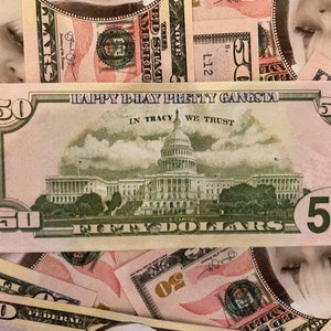 May include: A fifty-dollar bill with the text "HAPPY B-DAY PRETTY GANGSTA" and "IN TRACY WE TRUST" printed on it. The bill features the U.S. Capitol building and is surrounded by other fifty-dollar bills.