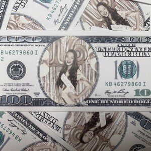 May include: A custom $100 bill with a photo of a young woman wearing a "Sweet 16" sash, surrounded by balloons. The bill's design includes the text "ONE HUNDRED DOLLARS" and the Federal Reserve Note seal. The background features other $100 bills.