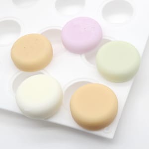 May include: A white silicone mold with 12 round cavities, filled with five different colored round soaps. The soaps are light brown, light yellow, white, light green, and light purple.