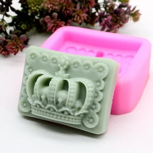 以下が含まれることがあります： 王冠のデザインの石鹸を作るためのピンクのシリコンモールド。モールドが開いており、王冠のデザインの緑色の石鹸バーが入っています。