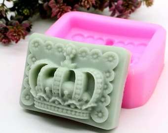 May include: A pink silicone mold for making soap with a crown design. The mold is open and a green soap bar with a crown design is inside.