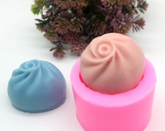 May include: Two silicone molds for making rose-shaped soap. One mold is pink and the other is blue. The pink mold has a rose-shaped soap inside.