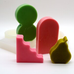 Pu&ograve; includere: Un set di cinque stampi in silicone per realizzare candele. Gli stampi hanno la forma di una pera, un rettangolo con gradini, un rettangolo alto e due cerchi collegati tra loro. Gli stampi sono verdi, rosa e marroni.