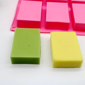May include: Two bars of handmade soap, one green and one yellow, sitting on a white surface. The soap bars are rectangular and have a smooth, glossy finish.