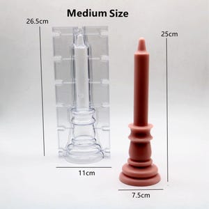 Może przedstawiać: Przezroczysty plastikowy foremka do świec z podstawą i wysokim, smukłym kształtem świecy. Obok znajduje się gotowa r&oacute;żowa świeca z podstawą i wysokim, smukłym kształtem. Foremka ma 11 cm wysokości i 26,5 cm szerokości. Świeca ma 7,5 cm szerokości i 25 cm wysokości. Rozmiar średni.
