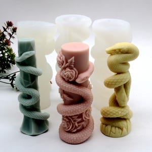 Puede incluir: Moldes de velas en varios colores y diseños. Uno es verde con una serpiente, otro es rosa con rosas y una serpiente, y un tercero es amarillo con una serpiente. Los moldes son para hacer velas decorativas.