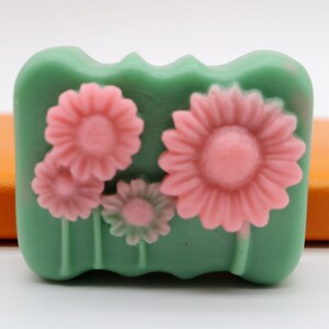 Puede incluir: Una pastilla de jab&oacute;n verde con un dise&ntilde;o floral. El jab&oacute;n presenta cuatro flores rosas con tallos y hojas verdes.