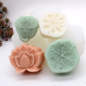 May include: Four handmade soap bars with lotus flower designs. The soaps are in shades of green, white, and pink.
