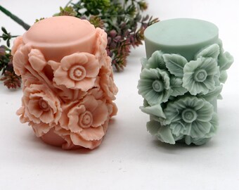 May include: Two cylindrical candles decorated with floral designs. One candle is pink with white flowers and the other is green with white flowers.