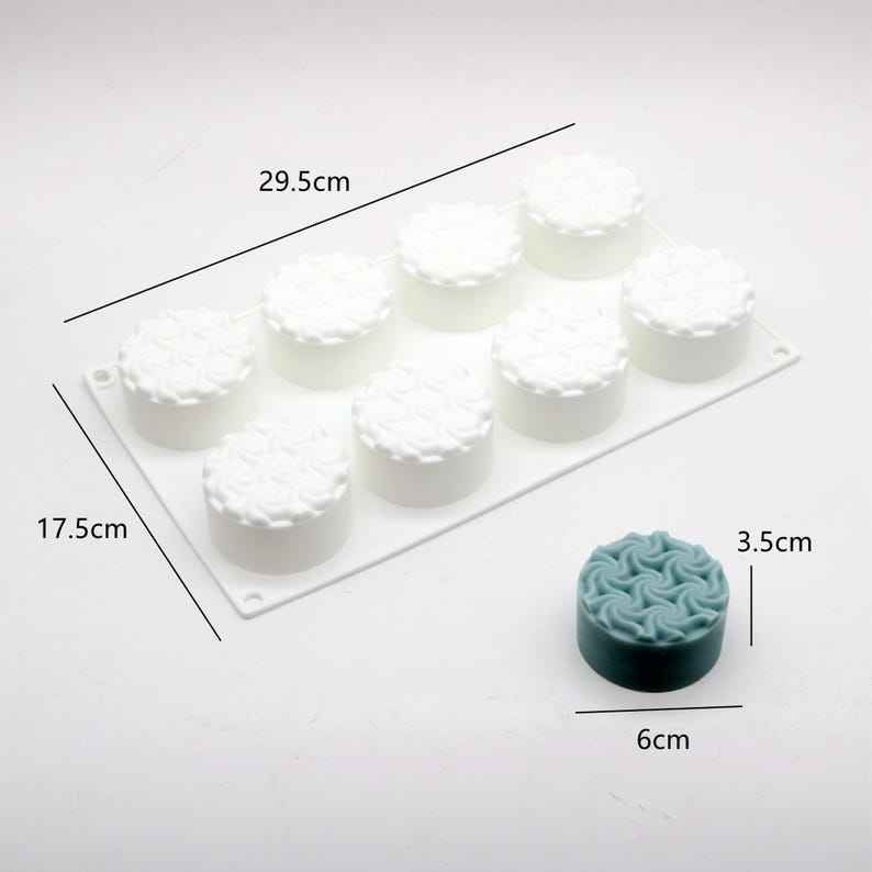 May include: A white silicone mold, 11.6 inches long and 6.9 inches wide, with eight round cavities, each with a floral design. A teal-colored, 2.4-inch diameter, 1.4-inch tall, finished product is shown next to the mold.