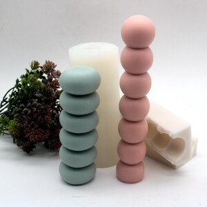 May include: Two silicone molds for making candles. One mold is a stack of six round shapes in a light blue color. The other mold is a stack of six round shapes in a light pink color.