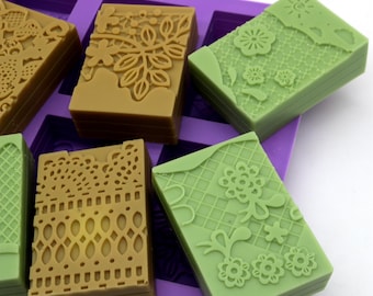 May include: A purple silicone mold with multiple rectangular cavities. Each cavity is filled with a stack of two rectangular bars of soap. The soap bars have a lace-like design and are in shades of green and brown.