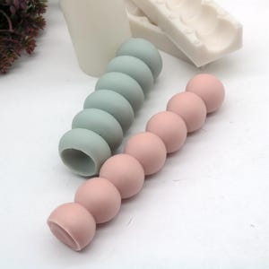 May include: Two silicone molds for making candles. One mold is light blue and the other is pink. Both molds are shaped like a series of connected spheres.
