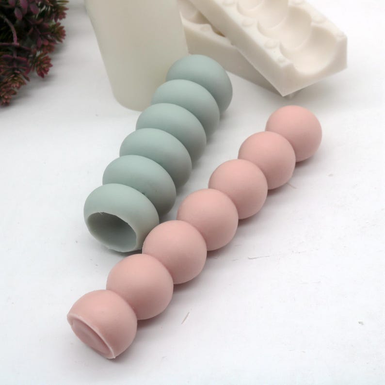 May include: Two silicone molds for making candles. One mold is light blue and the other is pink. Both molds are shaped like a series of connected spheres.