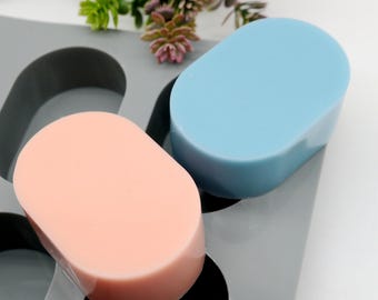 May include: Two oval-shaped soap bars in a silicone mold. One bar is light blue and the other is light pink.