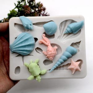 May include: Silicone mold with 10 different shapes of sea creatures and shells. The mold is white and has a light blue, pink, and green sea creature and shell designs.