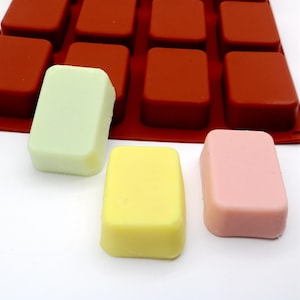 May include: Three rectangular bars of soap in different colors: light green, yellow, and pink. The soap bars are sitting on a white surface.