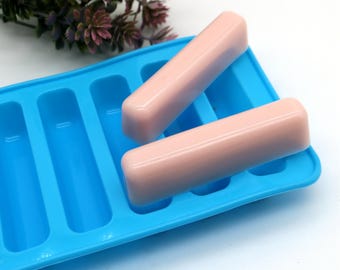 Puede incluir: Un molde de silicona azul con ocho cavidades rectangulares, dos de las cuales están llenas de barras de jabón rosas.