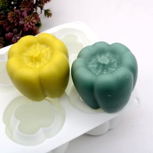 Puede incluir: Dos velas con forma de pimiento, una amarilla y otra verde, en un molde de silicona blanco.