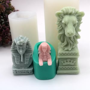 May include: Three silicone molds for making candles. The molds are green and feature a lion head, a seated pharaoh, and a standing pharaoh. The lion head mold has a base with a crown design. The pharaoh molds have the word "EGYPT" on the base.