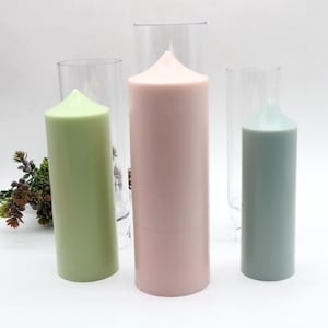 Może przedstawiać: Trzy świece w przezroczystych plastikowych pojemnikach. Świece są zielone, różowe i niebieskie.