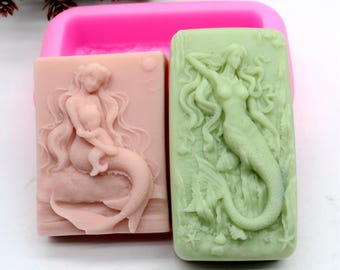 May include: Two silicone molds for making soap bars. The molds are rectangular and feature mermaid designs. One mold is pink and features a mermaid sitting on a rock with a baby mermaid. The other mold is green and features a mermaid swimming with her tail in the water.