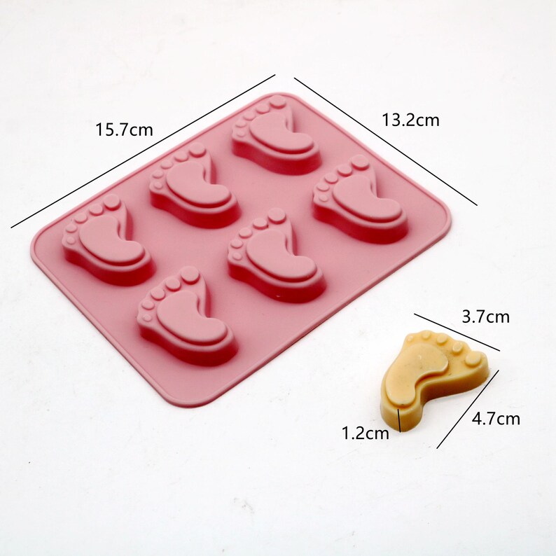 May include: Pink silicone mold with six baby foot shapes, measuring 15.7 inches by 13.2 inches. A single yellow baby foot shaped soap is shown next to the mold, measuring 4.7 cm by 3.7 cm.