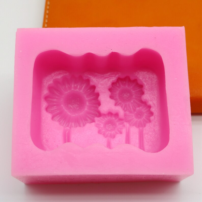 Puede incluir: Molde de silicona rosa con tres dise&ntilde;os de girasoles en relieve. El molde es rectangular y tiene una superficie lisa.