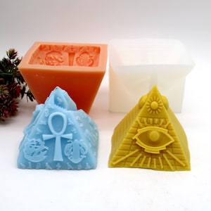 May include: Three silicone moulds for making pyramid-shaped candles. The moulds are in different colours: orange, white, and blue. The blue mould has an ankh symbol on it, the white mould is plain, and the orange mould has a design of a pyramid with an eye on it.