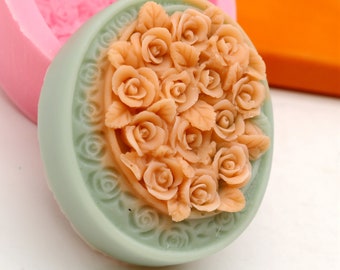 May include: A round, light green soap mold with a detailed floral design. The mold features a raised design of a bouquet of peach-colored roses.