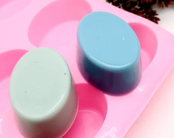 May include: A pink silicone mold with two oval-shaped soap bars. One soap bar is light blue and the other is light green.