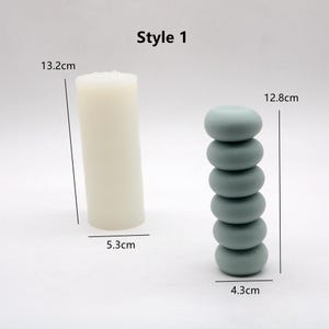 May include: Style 1 candle holder set with two options. The first option is a white cylindrical candle holder measuring 13.2 inches tall and 5.3 inches wide. The second option is a stack of six light blue round candle holders measuring 12.8 inches tall and 4.3 inches wide.