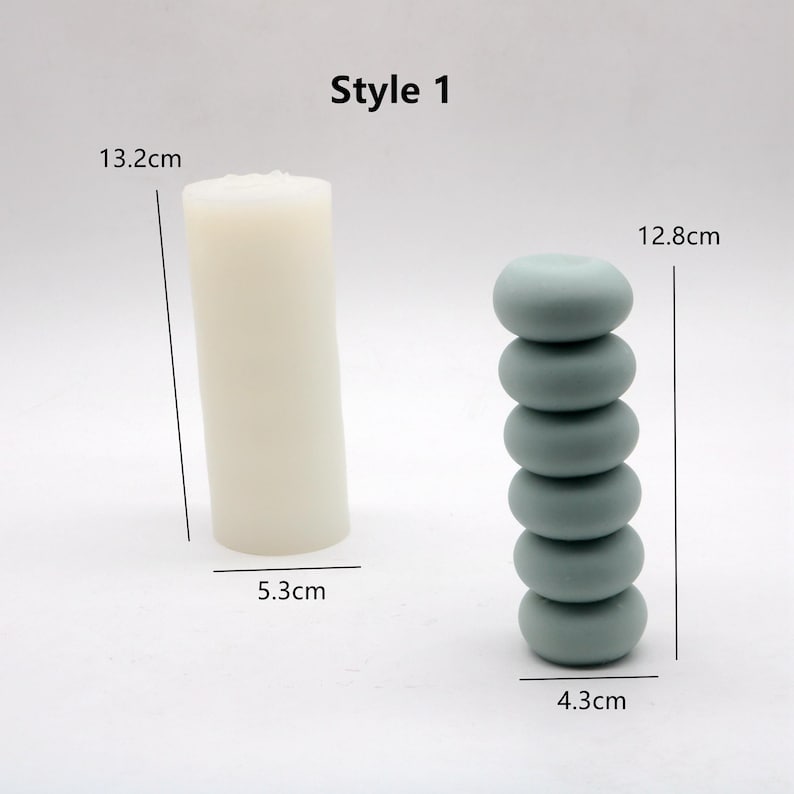 May include: Style 1 candle holder set with two options. The first option is a white cylindrical candle holder measuring 13.2 inches tall and 5.3 inches wide. The second option is a stack of six light blue round candle holders measuring 12.8 inches tall and 4.3 inches wide.